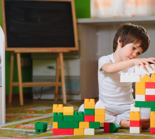 child little boy playing with wooden cubes toys in nursery at home or daycare center